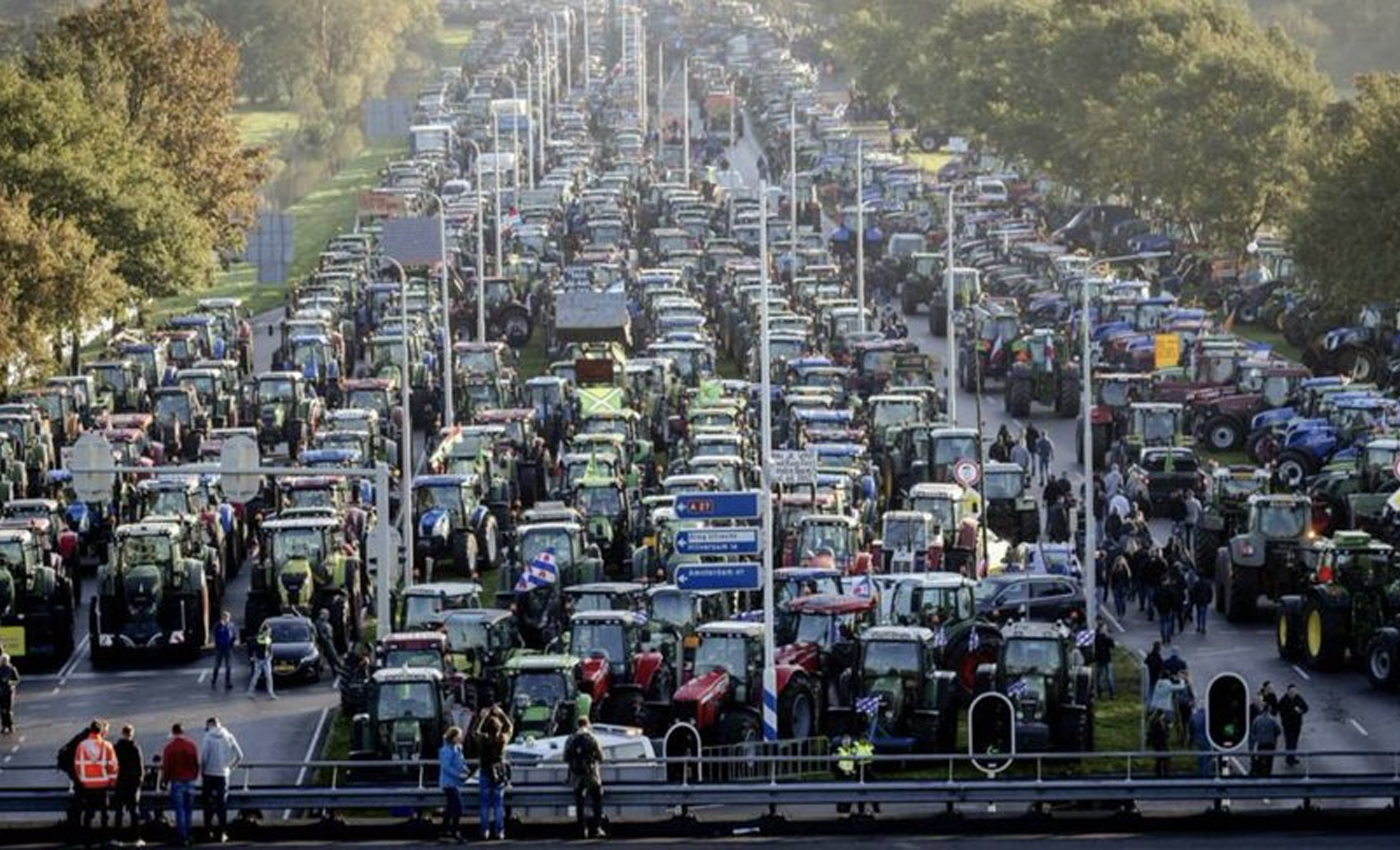 The image shows farmers blocking the highway with tractors in the Netherlands to protest against government plans to cut nitrogen emissions.