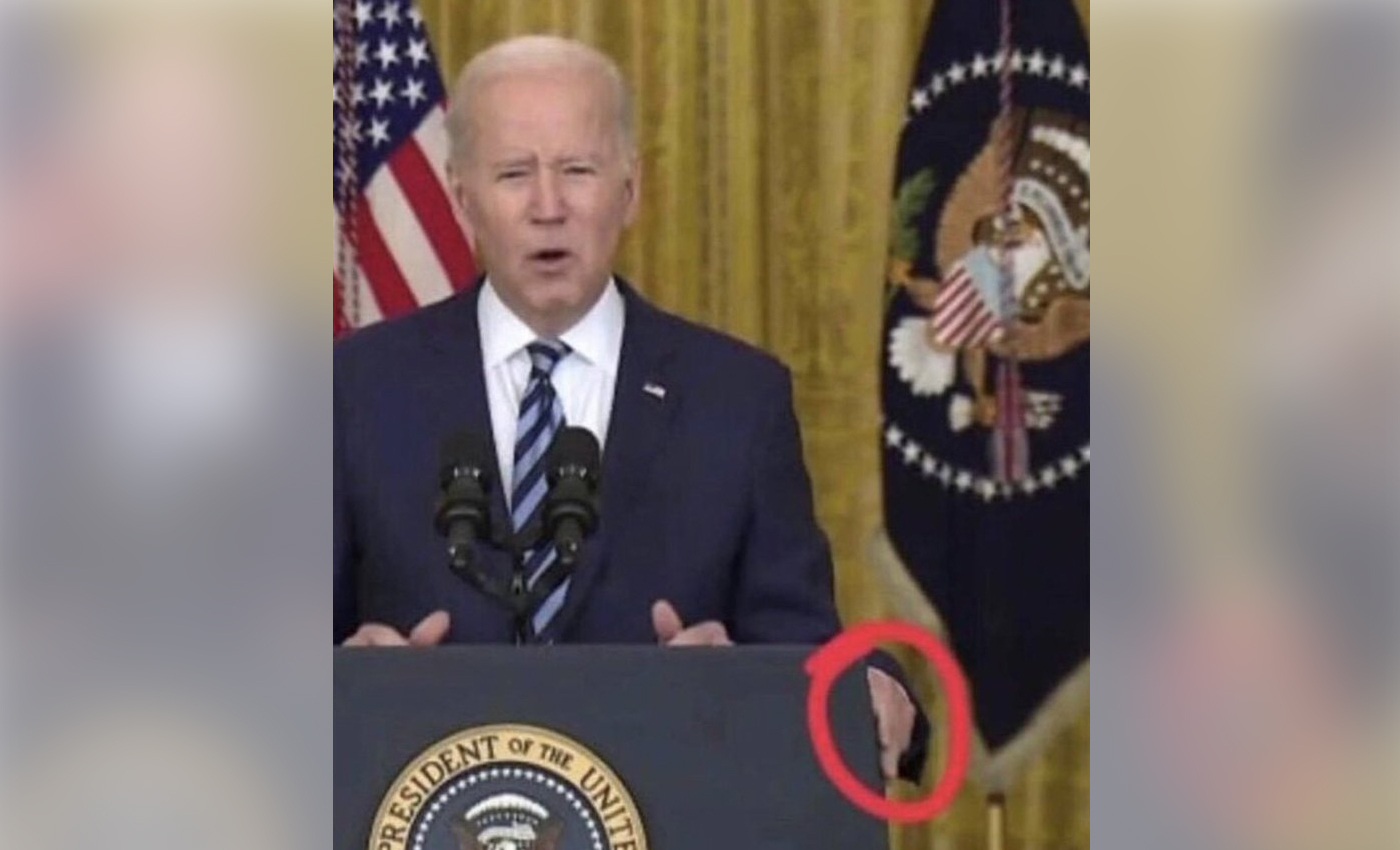 An image shows Biden placing a third hand on the podium during a press conference.